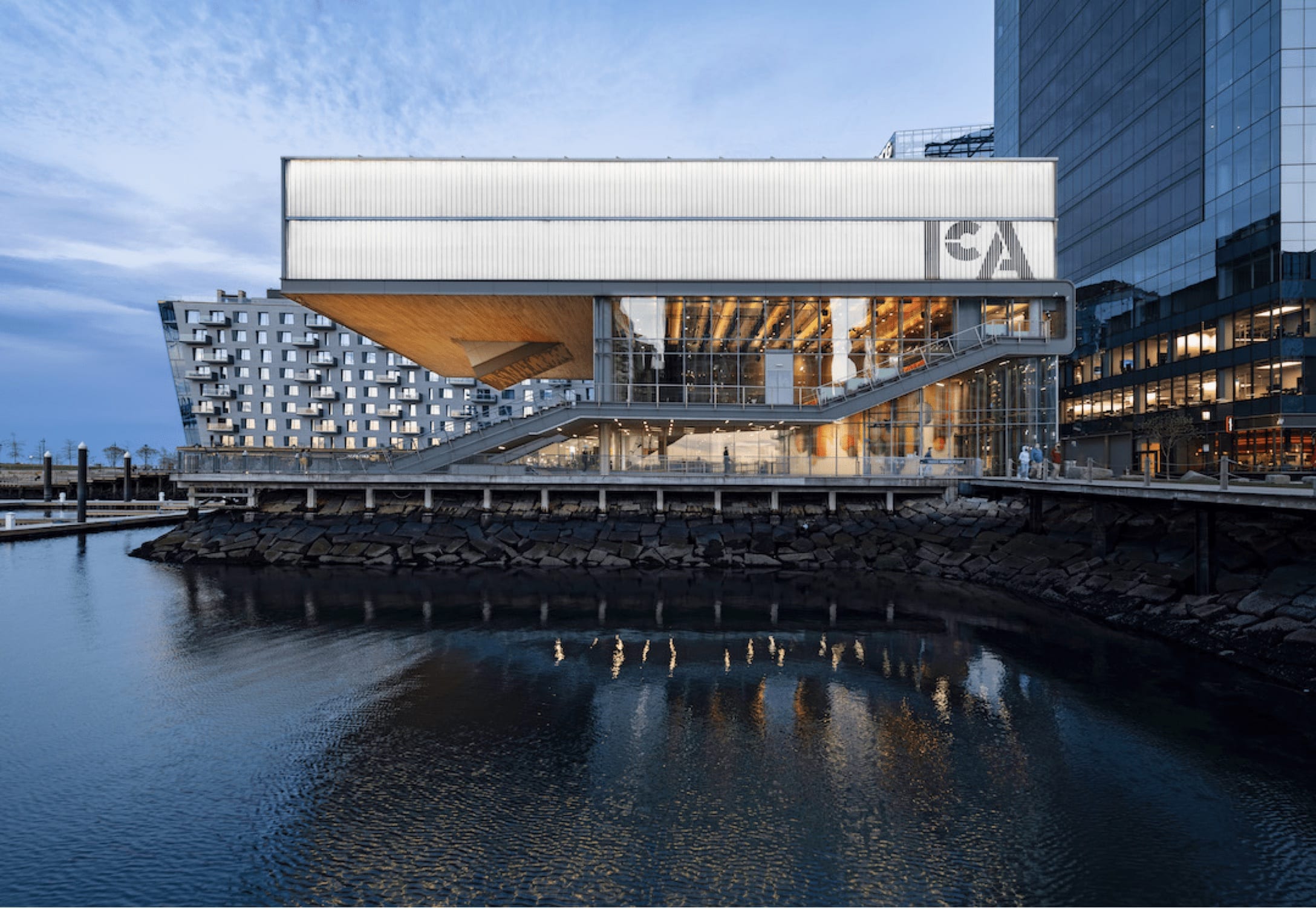 The ICA building at dusk, featuring a glowing top level cantilevered over Boston Harbor and glass-walled theater and lobby spaces lit from within.