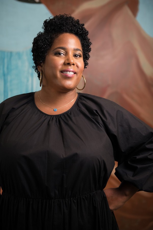 Rashida Bumbray, a medium-dark-skinned woman with short black hair, wearing a black dress and good hoop earrings, smiling..